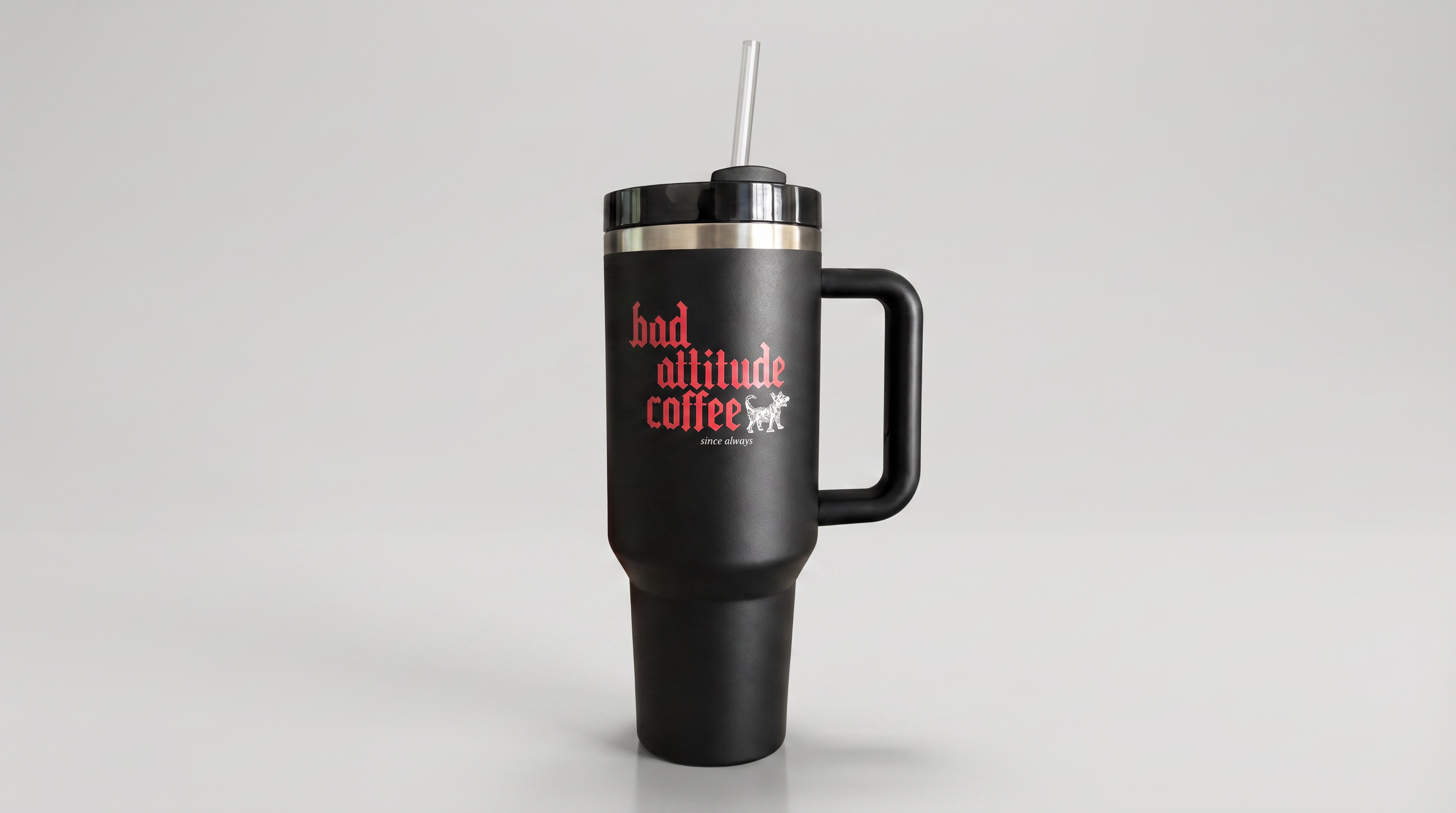 A matte black insulated travel tumbler with a handle, lid, and straw, featuring the red and white text 'bad attitude coffee' on the front, set against a neutral gray background.